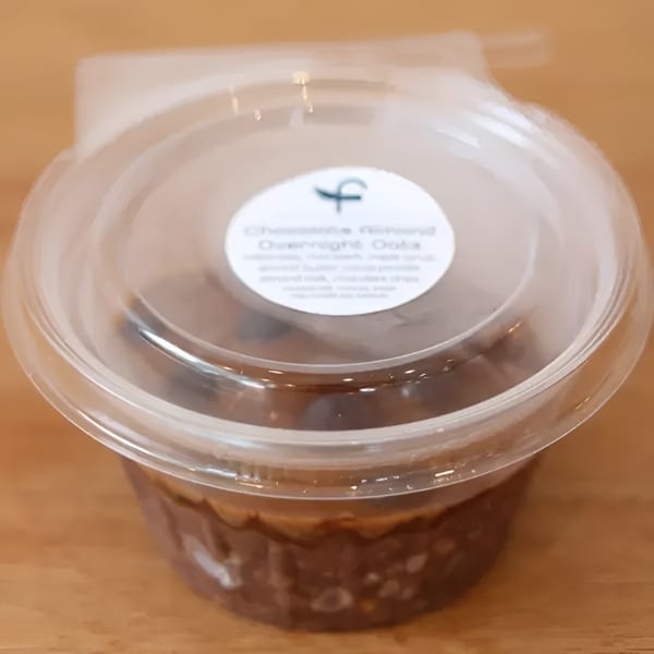 Chocolate Almond Overnight Oats in a clear plastic container with a white label on a wooden surface.