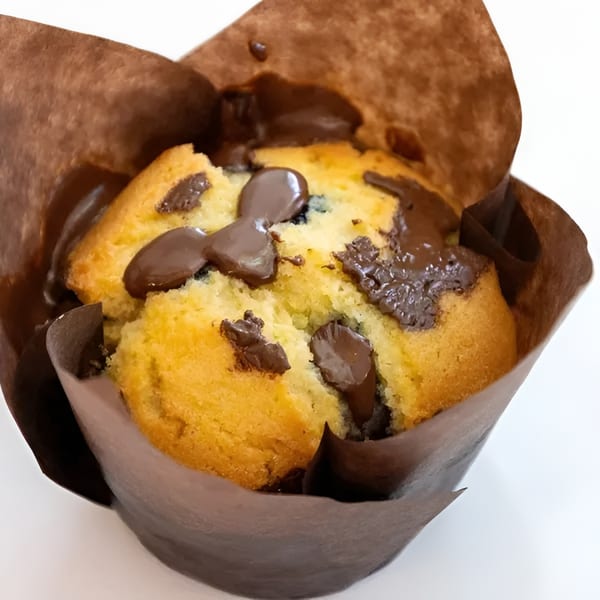 Close-up of a golden-brown muffin with melted chocolate chips in a brown paper liner.