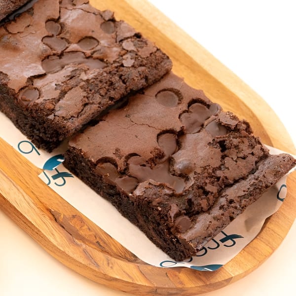 Two rich chocolate brownies with chocolate chips on a wooden tray with branded paper.