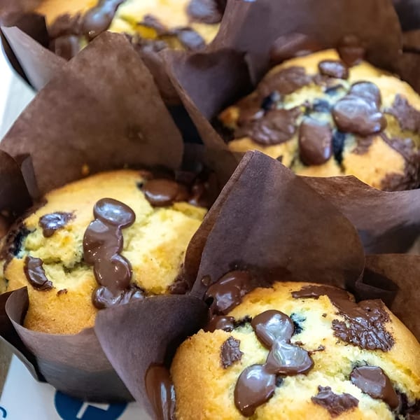 Close-up of several golden muffins with melted chocolate chips in brown paper liners.