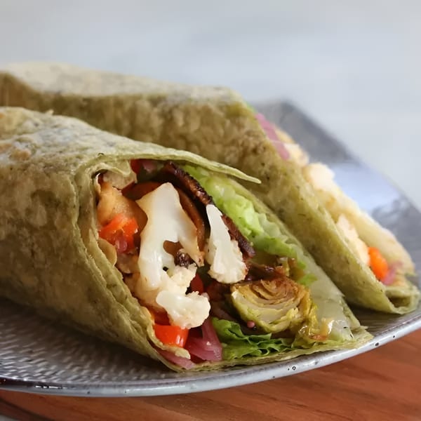 Two green wraps filled with cauliflower, red peppers, and lettuce on a gray plate.
