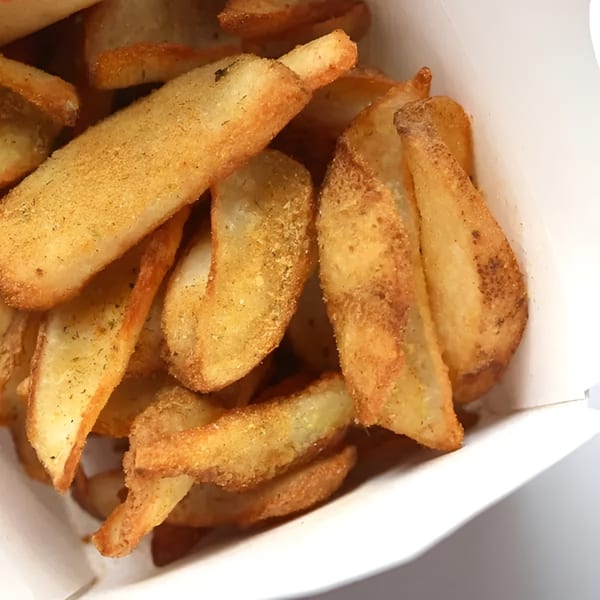 Close-up of golden brown potato wedges seasoned with spices, served in a white paper container.