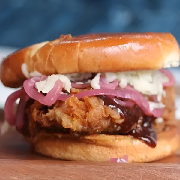 Crispy fried chicken sandwich with barbecue sauce, pickled red onions, and coleslaw on a brioche bun.
