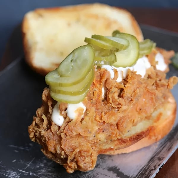 Crispy fried chicken sandwich with white sauce and pickle slices on a toasted bun.