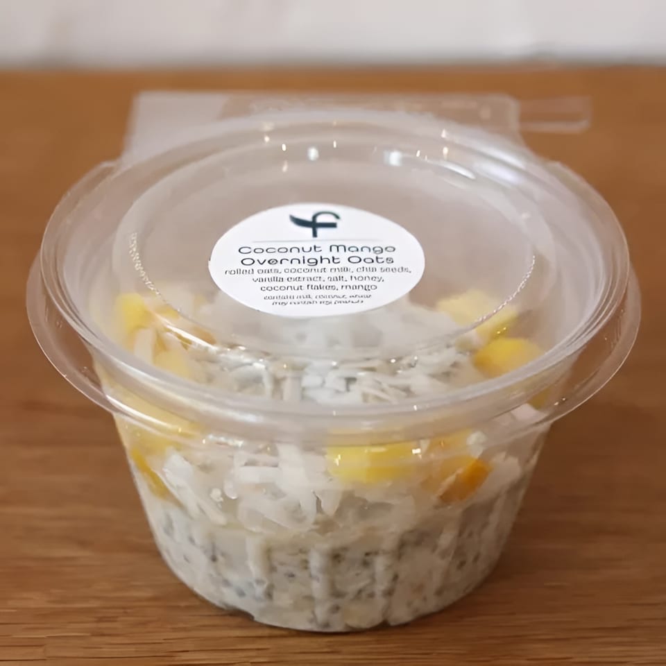 Coconut Mango Overnight Oats in a clear plastic container with a label on a wooden surface.