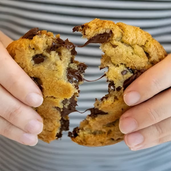 Hands pulling apart a warm chocolate chip cookie, revealing gooey melted chocolate inside.