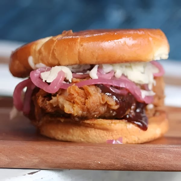 Crispy fried chicken sandwich with barbecue sauce, coleslaw, and pickled red onions on a brioche bun.