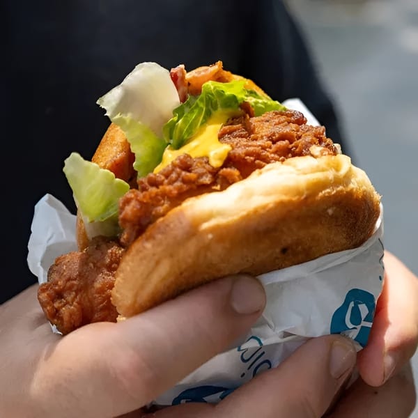 Hands holding a fried chicken sandwich with lettuce, cheese, and sauce on a bun.