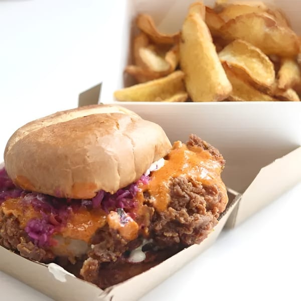 Crispy chicken sandwich with red cabbage slaw and orange sauce, with potato wedges in a box.