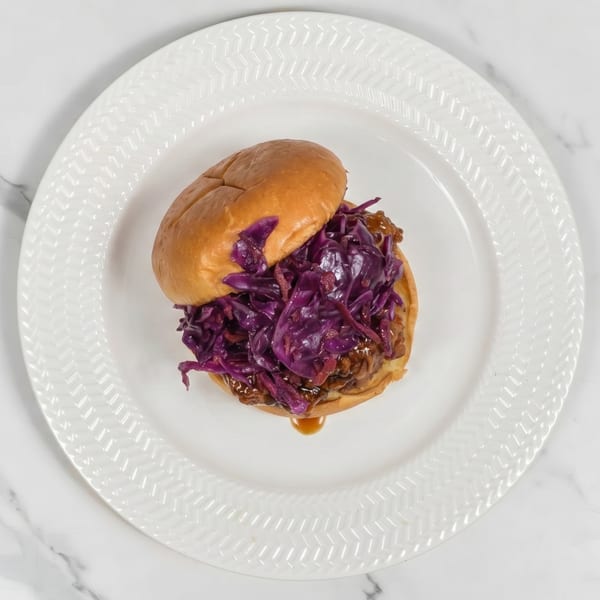 Pulled pork sandwich with purple cabbage slaw on a white plate.